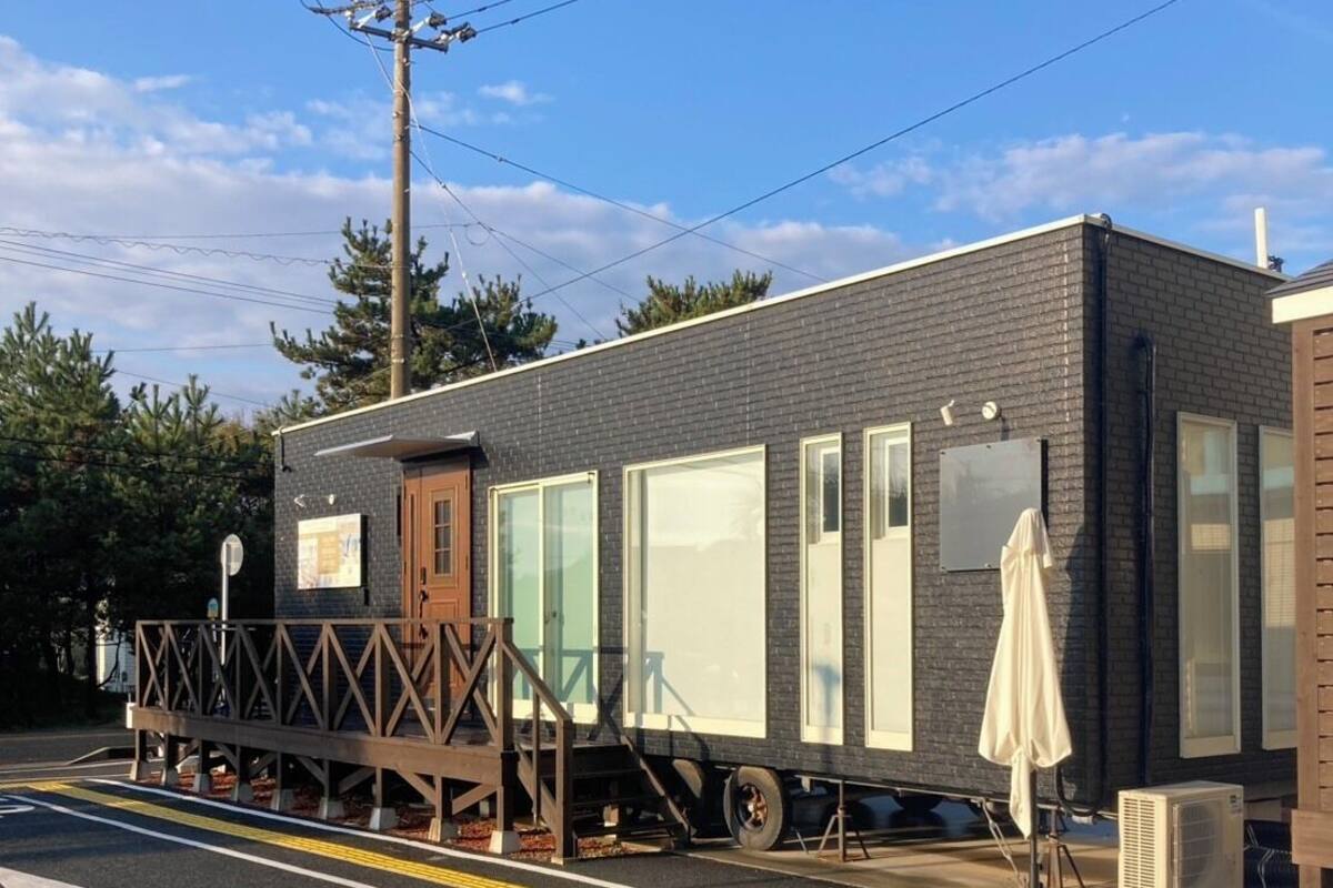 A mobile home with a small porch and a covered outdoor area, parked on a street with a clear sky.