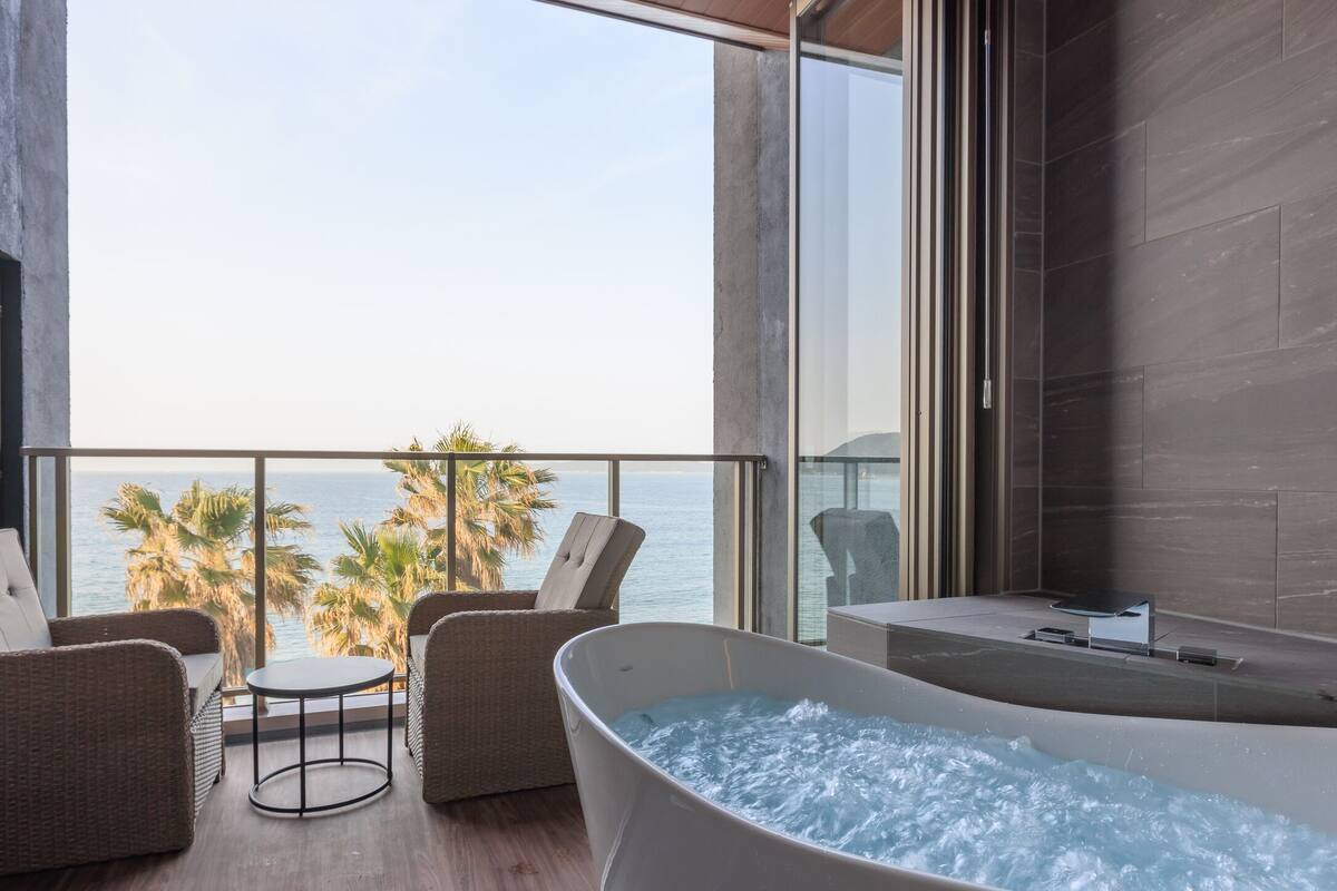 A balcony with a jacuzzi, wicker chairs, and a view of the ocean.