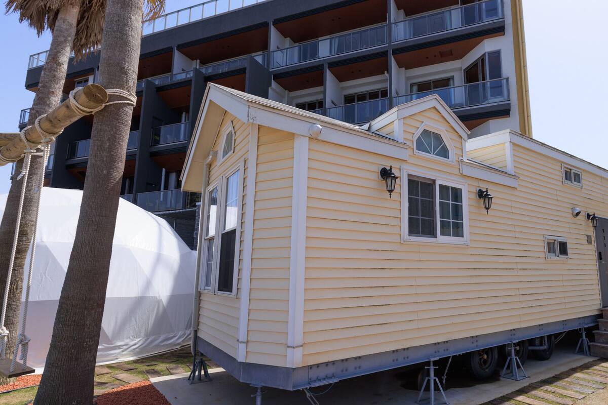A mobile home with a gabled roof, positioned on a concrete pad with steps leading up to it.