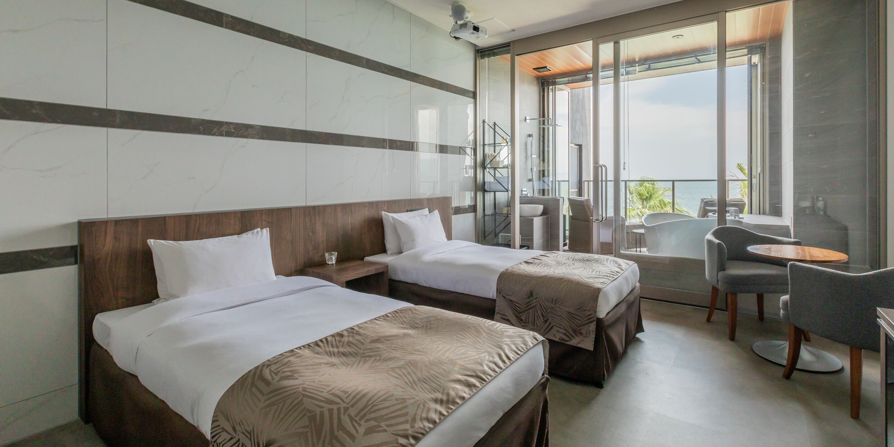 A hotel room with two beds, a balcony with a table and chairs, and a view of the sea.