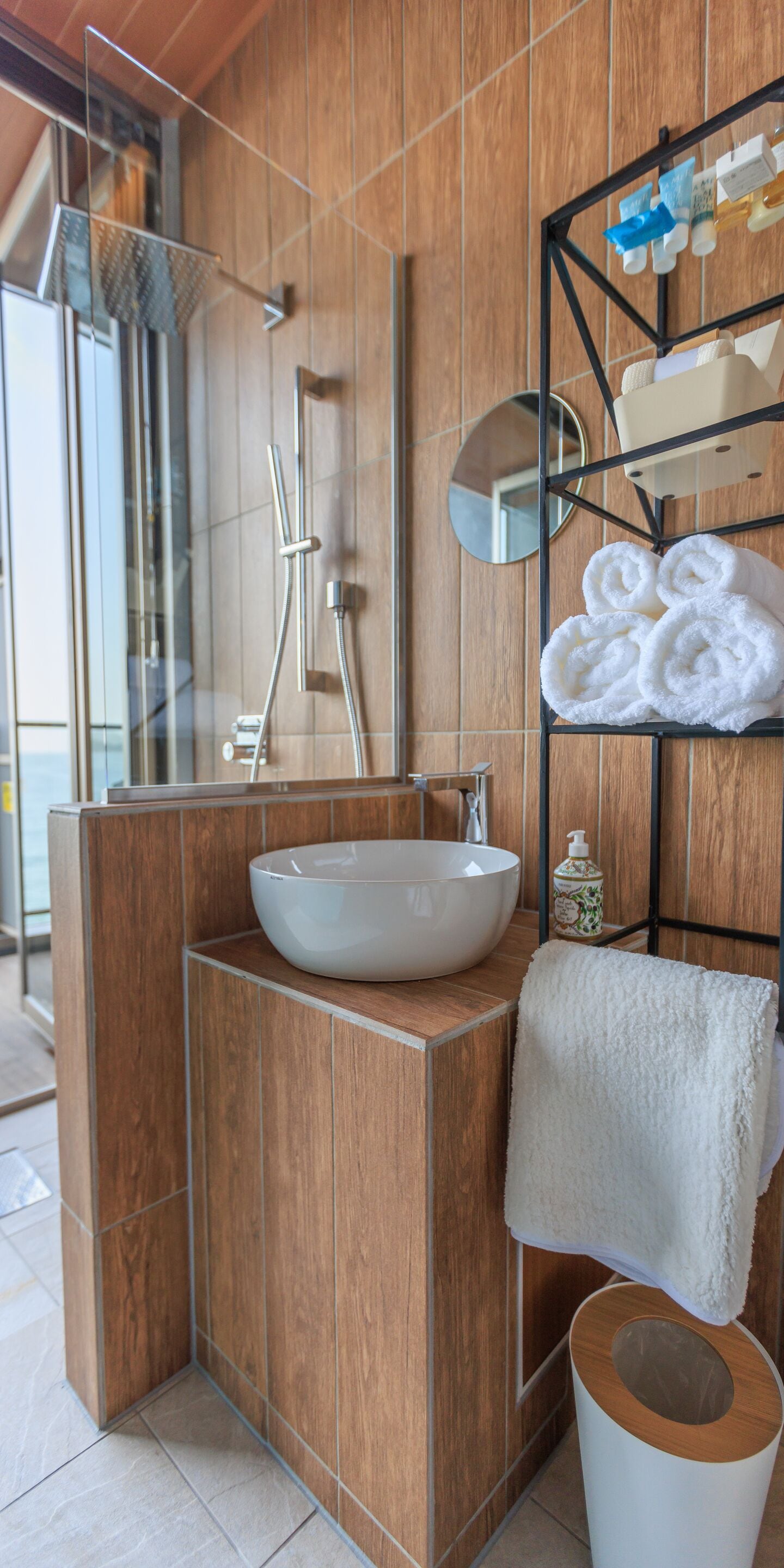 A modern bathroom with a wooden vanity, a white sink, a mirror, and a towel rack.