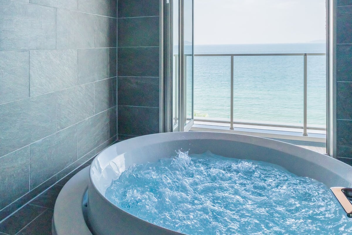 A modern bathroom with a large bathtub, a view of the sea, and a wooden ceiling.
