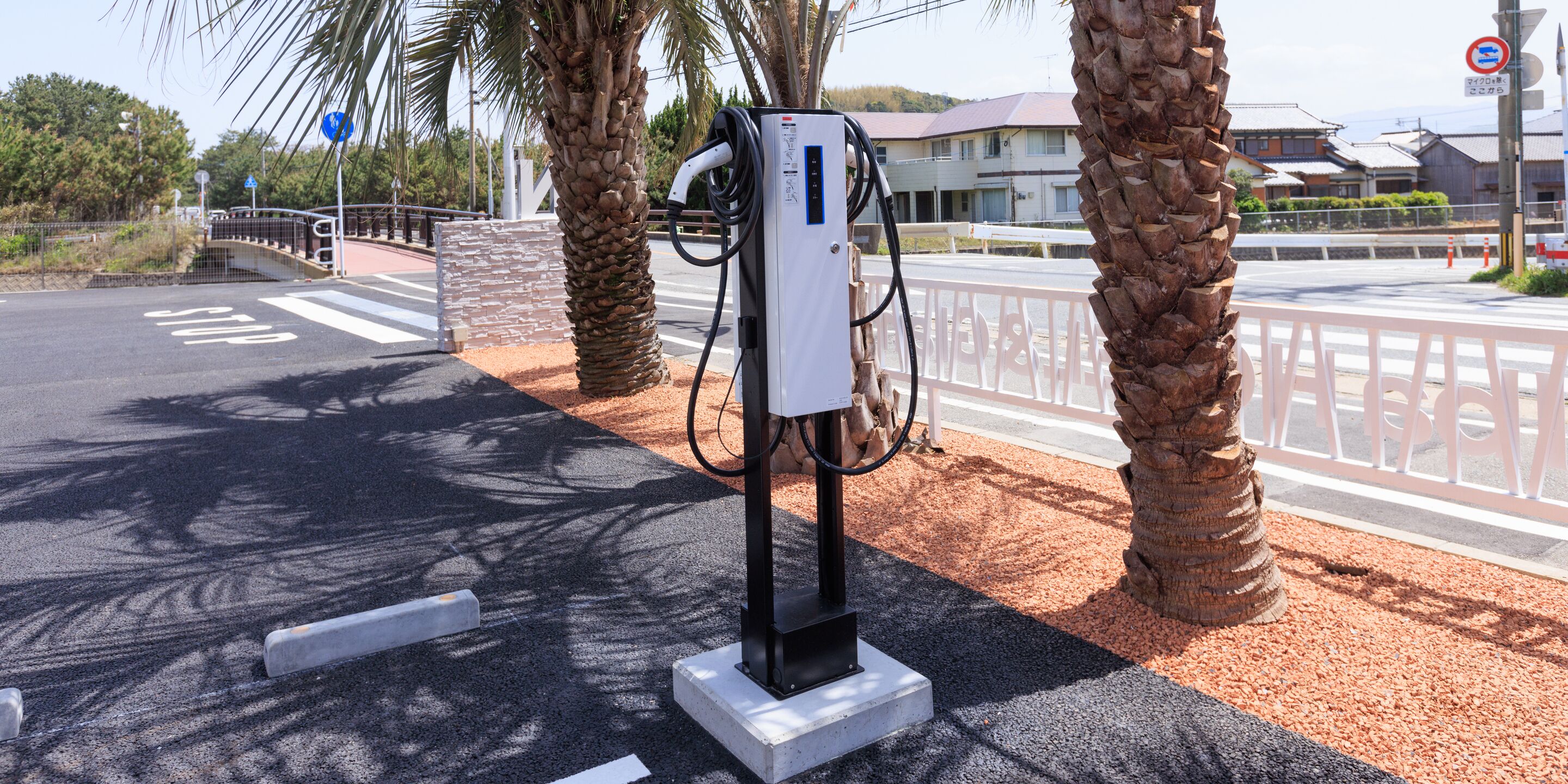 A charging station for electric vehicles, palm trees, and a pedestrian crossing.