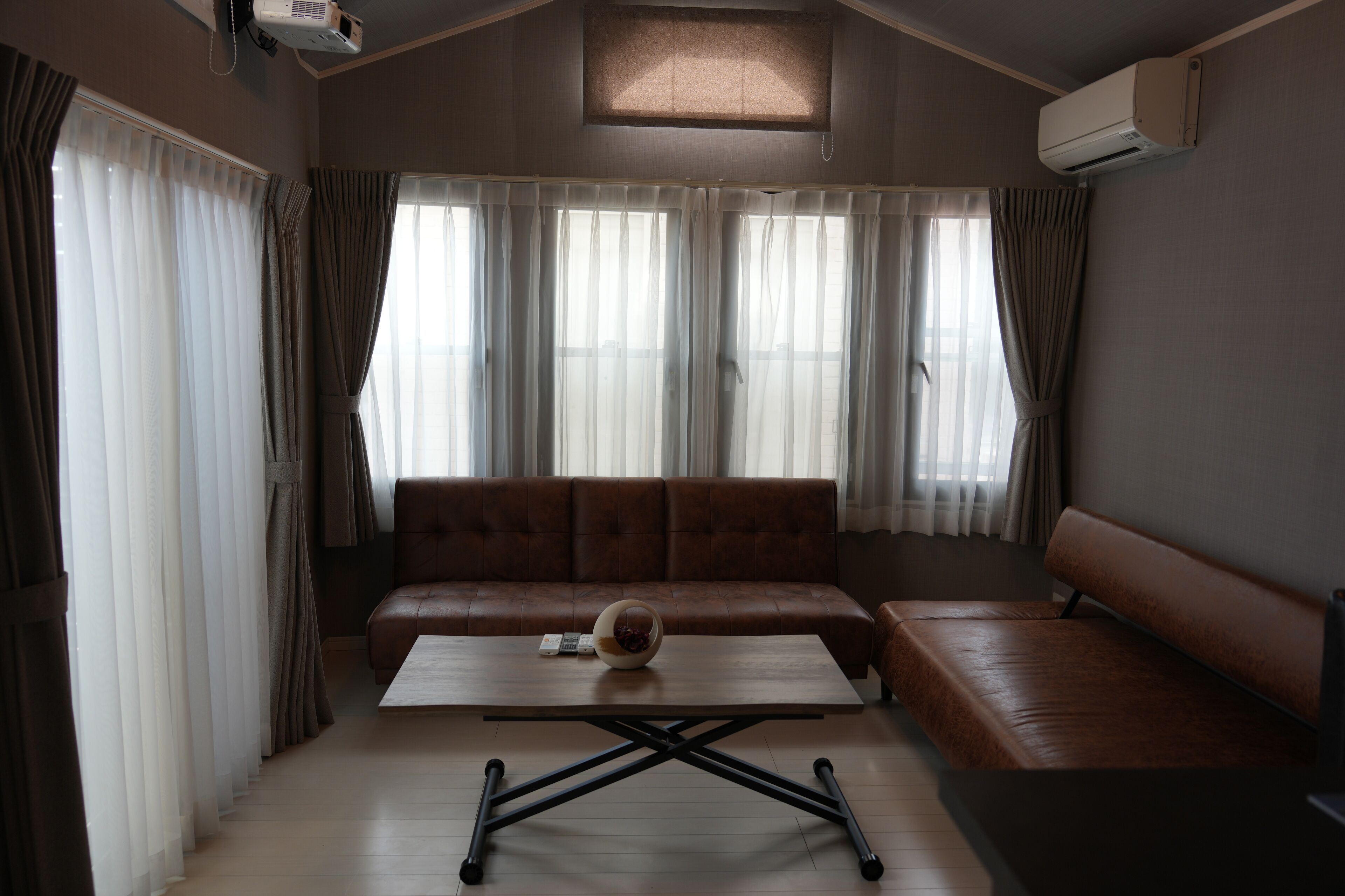 A room with a brown leather sofa, a wooden coffee table, and a large window with curtains.