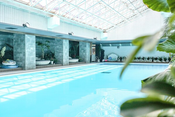 Une piscine intérieure dotée d’un plafond en verre transparent, de plantes en pot et d’un sol carrelé.