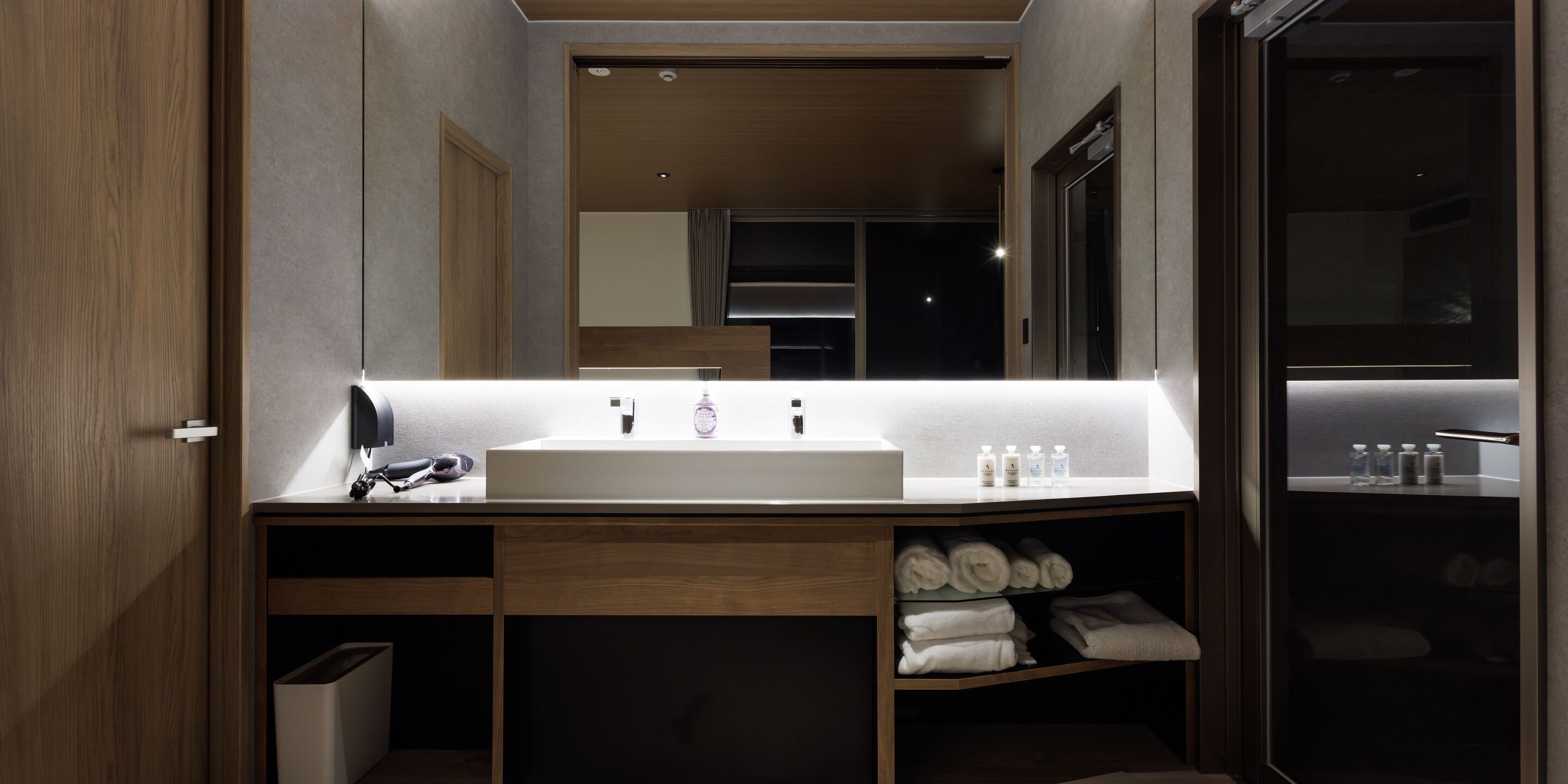 A modern bathroom with a large mirror, a white sink, and built-in towel storage.