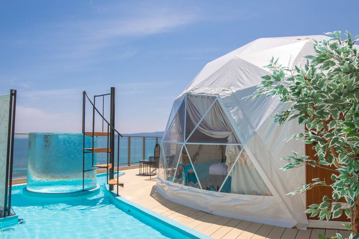 A pool area with a slide, a covered seating area, and a view of the sea.