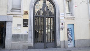 Une entrée d’immeuble avec un grand portail métallique en arc de cercle, portant le numéro 4, une plaque avec des armoiries et une affiche publicitaire pour un site web.
