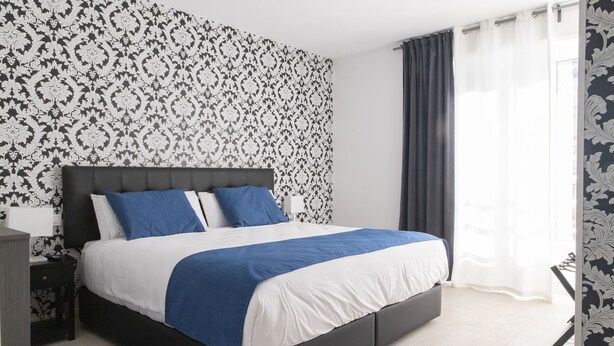 Une chambre à coucher moderne avec un grand lit, une tête de lit sombre et un papier peint à motifs.