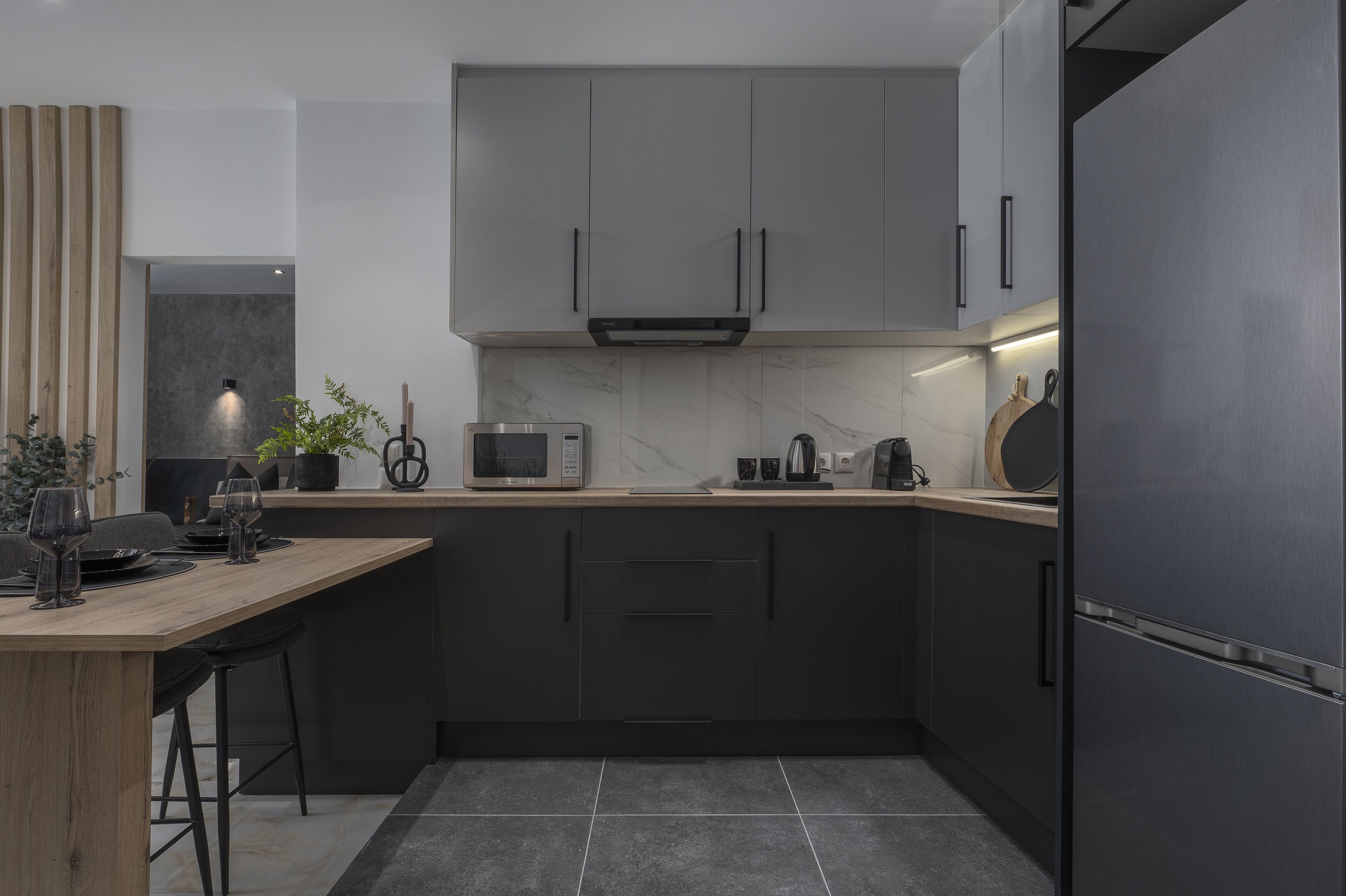A modern kitchen with dark cabinets, a marble countertop, and a built-in microwave.