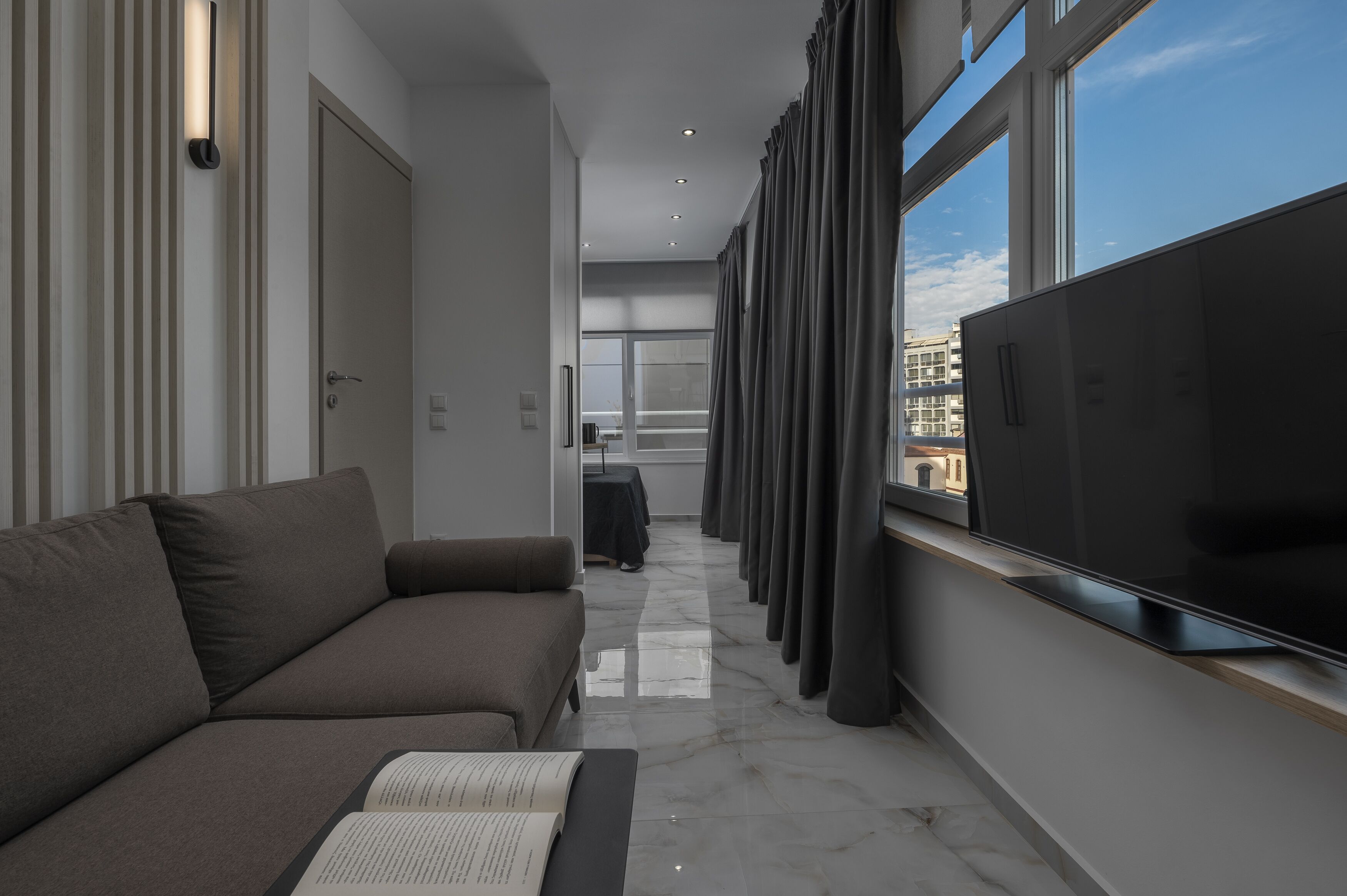 Un salón moderno con sofá, televisor de pantalla plana y vistas de la ciudad a través de amplias ventanas.