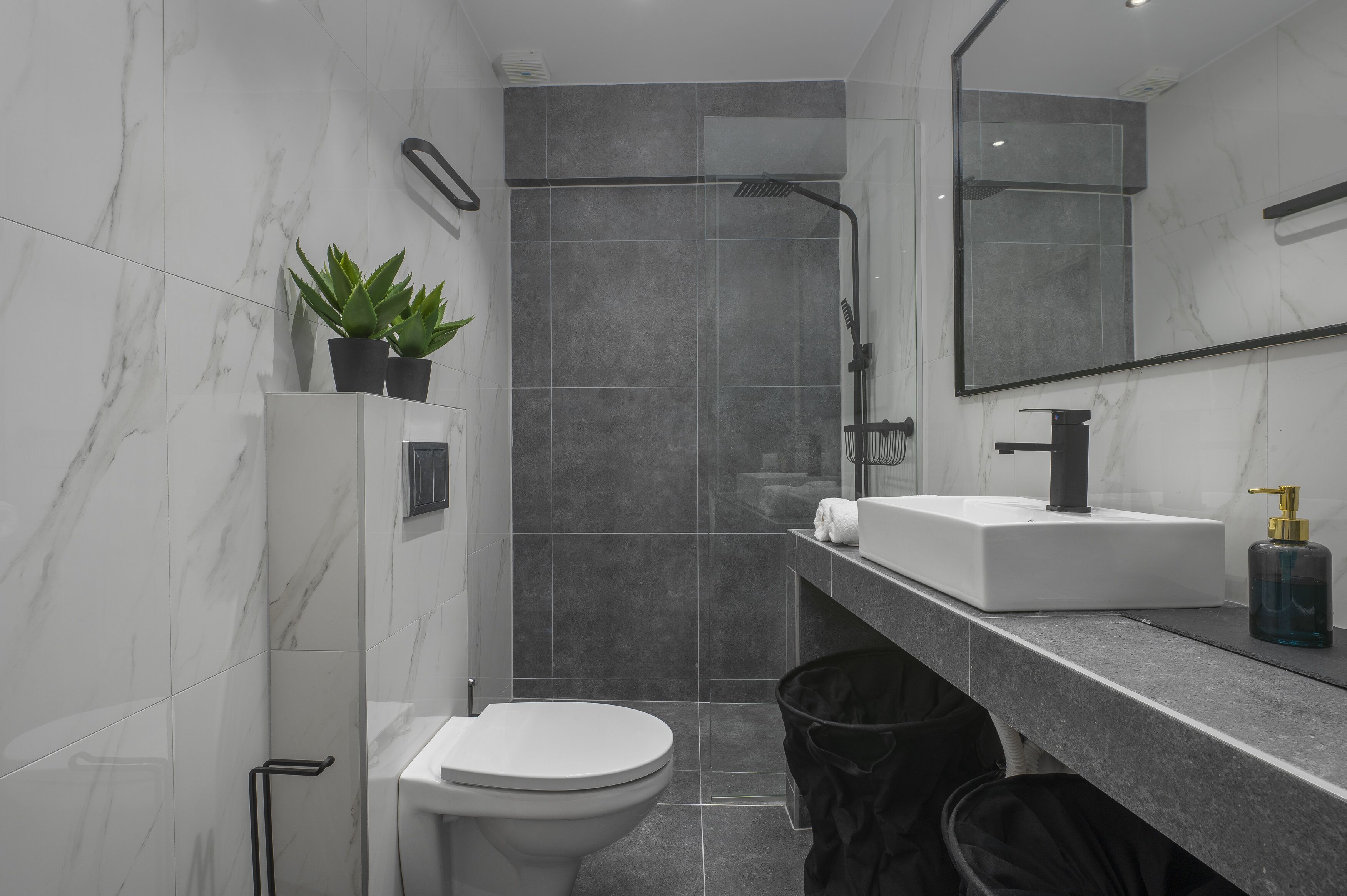 Un bany modern amb un vàter blanc, un lavabo amb aixeta daurada, un mirall i una zona de dutxa.