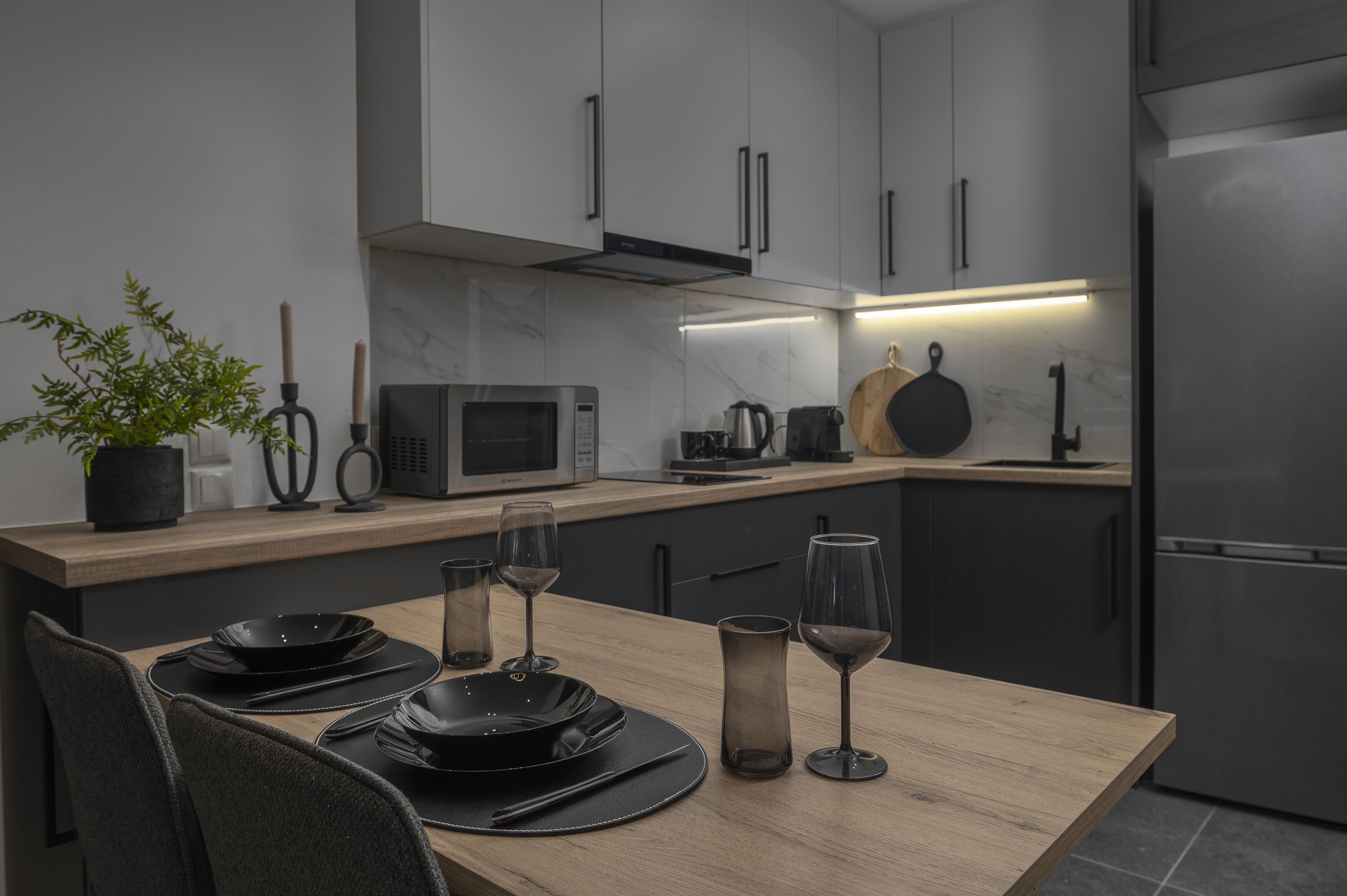 A modern kitchen with a wooden countertop, a built-in microwave, a kettle, and a stainless steel refrigerator.