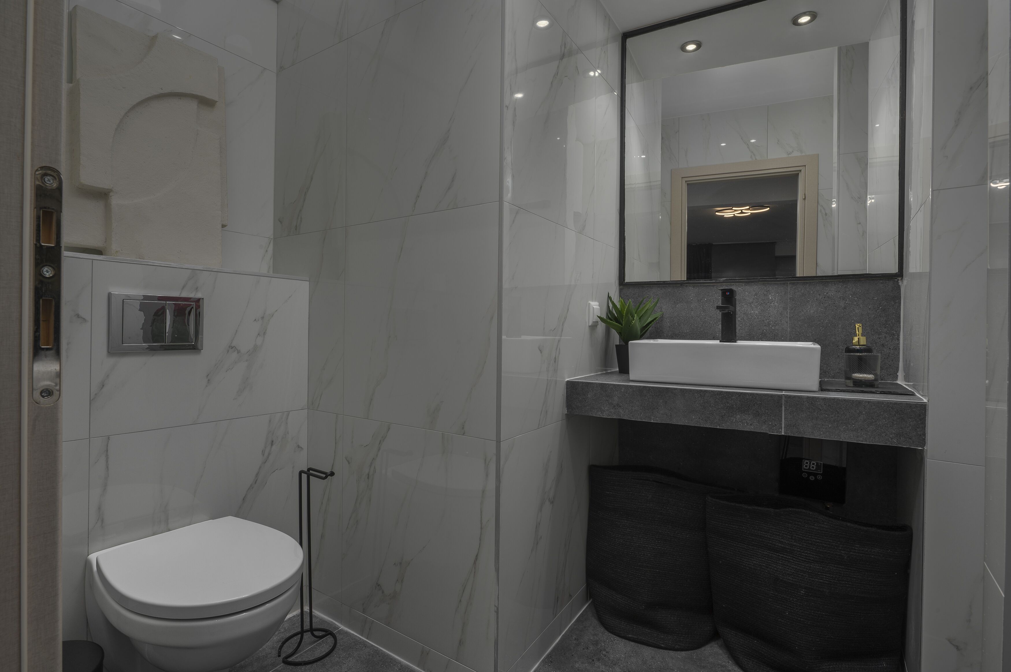 Une salle de bain moderne avec des toilettes blanches, un lavabo surmonté d’un miroir et un espace douche.