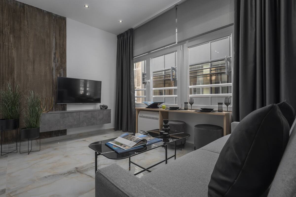 Een moderne woonkamer met een bank, een salontafel, een flatscreen-televisie en een raam met gordijnen.