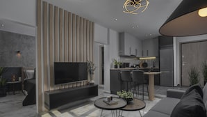 Een moderne woonkamer met een flatscreen televisie, een bank, een salontafel en een eethoek, met een keuken op de achtergrond.
