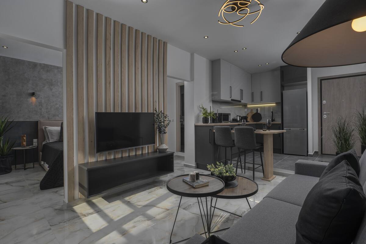 Een moderne woonkamer met een flatscreen televisie, een bank, een salontafel en een eethoek, met een keuken op de achtergrond.