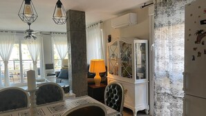 Un coin repas avec une table dressée pour quatre personnes, un lustre, un buffet aux portes vitrées et un réfrigérateur.