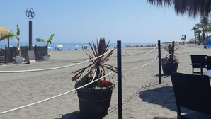 Une plage agrémentée d’une structure à toit de chaume, de plantes en pot et d’une barrière en corde.