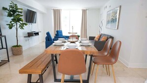 A dining area with a wooden table, four chairs, and a bench. A television is mounted on the wall, and there is a plant in the corner. - 2BR Heart of Brickell W/ Pool, Hot Tub, and Gym! (Miami)