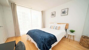 A bedroom with a bed, a laptop on a desk, and a window with curtains. - 2BR Heart of Brickell W/ Pool, Hot Tub, and Gym! (Miami)