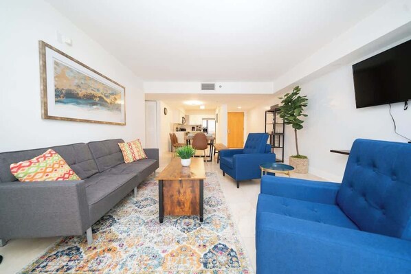 A modern living room with a grey sofa, a blue sofa, a wooden coffee table, and a colorful rug. - 2BR Heart of Brickell W/ Pool, Hot Tub, and Gym! (Miami)