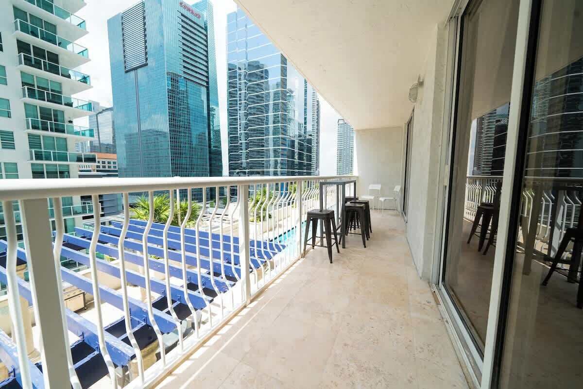 A balcony with a view of modern buildings, a railing, and a few chairs.
