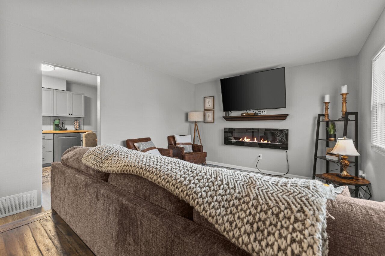 A living room with a sofa, a fireplace, a television, and a kitchen area visible through an open door.