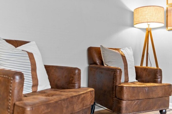 Two brown leather armchairs with striped pillows, a wooden floor lamp, and a white wall.