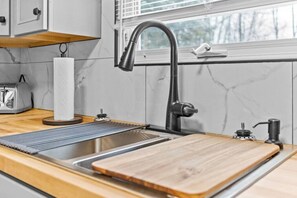 A modern kitchen with a stainless steel sink, wooden countertop, and a window with blinds. - Boho Chic Work Escape - 2-Bedroom, Close to Burlington/Airport (South Burlington)
