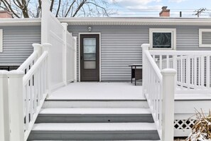 Une maison à deux étages, avec une façade grise, des balustrades blanches et une porte d’entrée.