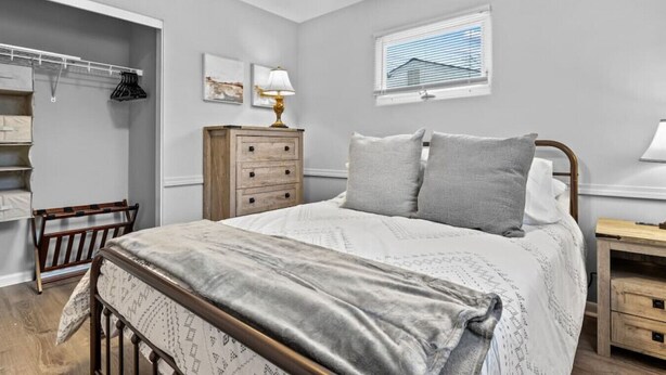 A bedroom with a bed, a wooden dresser, a nightstand, a window with blinds, and a coat rack. - Boho Chic Work Escape - 2-Bedroom, Close to Burlington/Airport (South Burlington)
