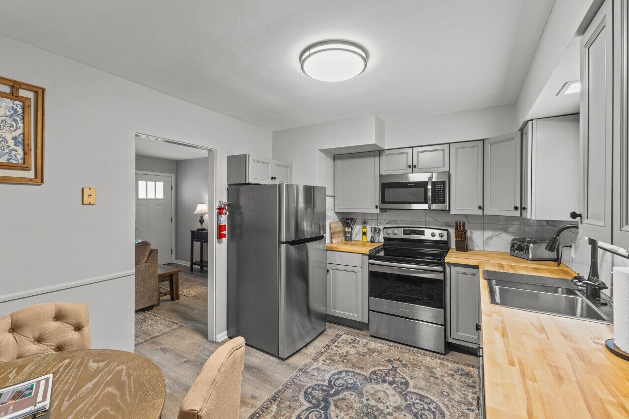 A modern kitchen with stainless steel appliances, a wooden countertop, and a patterned rug.