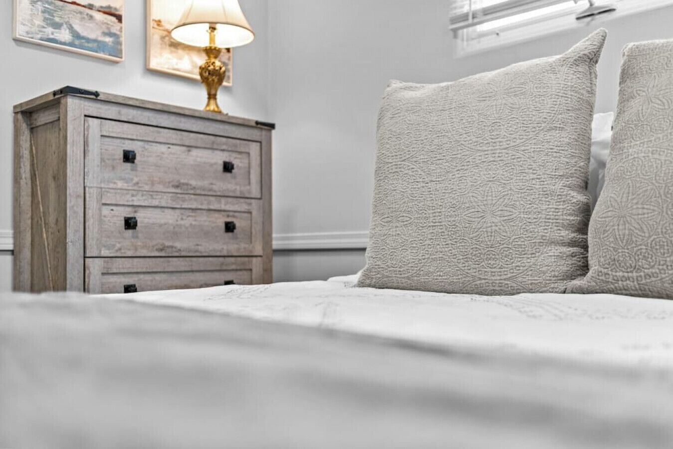 Un lit bien fait, avec un oreiller à texture intéressante et une table de chevet en bois sur laquelle se trouve une lampe.