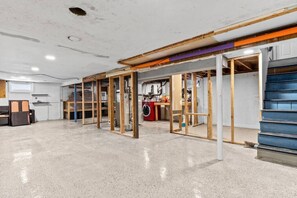 A spacious, unfinished basement with exposed wooden framing and a concrete floor.