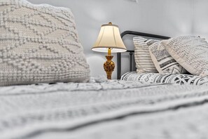 A bed with a white knitted blanket, a bedside lamp with a gold base, and patterned pillows.
