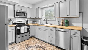 A modern kitchen with stainless steel appliances, white cabinetry, and a wooden countertop. - Boho Chic Work Escape - 2-Bedroom, Close to Burlington/Airport (South Burlington)