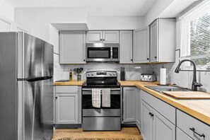 Una cocina moderna con electrodomésticos de acero inoxidable, armarios grises y encimera de madera.