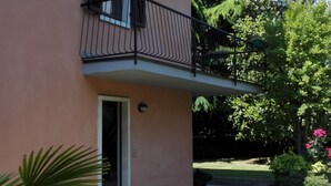 A two-story building with a balcony, a door, and a small garden area with grass and plants. - Flat with terrace, quiet and sunny,2 bike, air cond,bike storage (Riva del Garda)