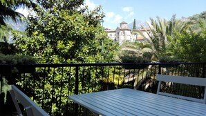 A balcony with a white table and chairs, surrounded by lush greenery and a view of a historic building with a tower. - Flat with terrace, quiet and sunny,2 bike, air cond,bike storage (Riva del Garda)