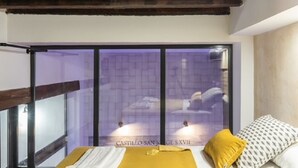 Ein Schlafzimmer mit einer großen Schiebeglasdoor zu einem Innenhof, einem Bett mit gelbem Kissen und einem Holzbalken an der Decke.
