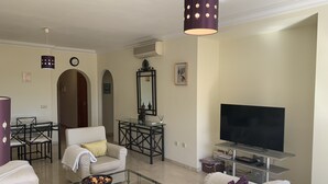 Ein Wohnzimmer mit Sofa, Couchtisch, Fernseher und einem Essbereich mit Stühlen und Tisch.