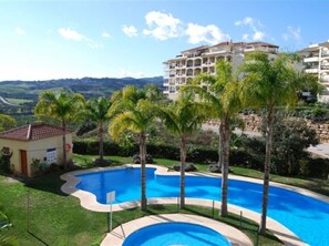 A swimming pool surrounded by palm trees, with a view of a large building in the background. - Spacious 2 Bed 2 Bath La Cala Hills Mijas - Prime Location (Mijas Costa)