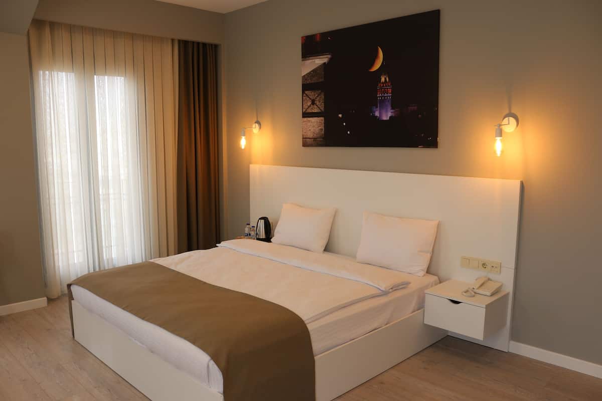 Una habitación de hotel con una cama grande, una mesita de noche con lámpara y un cuadro de un paisaje urbano en la pared.