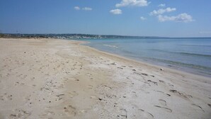 Ein sandiger Strand mit Fußspuren, die zum Wasser führen, ein klarer Himmel und eine entfernte Küstenlinie.