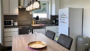 A modern kitchen with a dining table, chairs, a refrigerator, and a clock on the wall. - Sonnenweg 1 (Diemelsee)