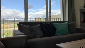 A living room with a sofa facing a large window overlooking a scenic landscape. - Sonnenweg 1 (Diemelsee)