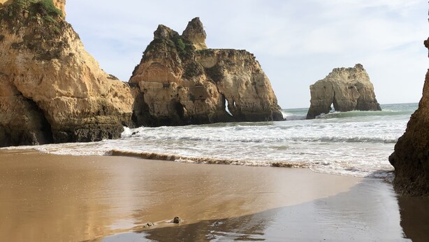 Une plage bordée de grandes formations rocheuses, où les vagues viennent se briser sur le rivage.