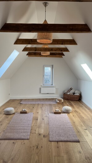 A spacious attic room with wooden beams, a skylight, a hanging light fixture, a window, and a small white radiator.