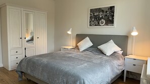 A bedroom with a bed, two bedside tables, a nightstand, a wardrobe, and a framed picture on the wall.